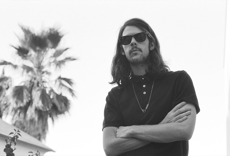 Estanislao López wearing a plain t-shirt and black sunglasses with a palm tree in the background